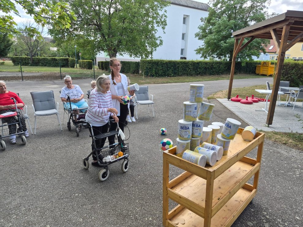Bewohnerin beim Dosenschießen. Praktikantin steht daneben und hält Ball in der Hand.