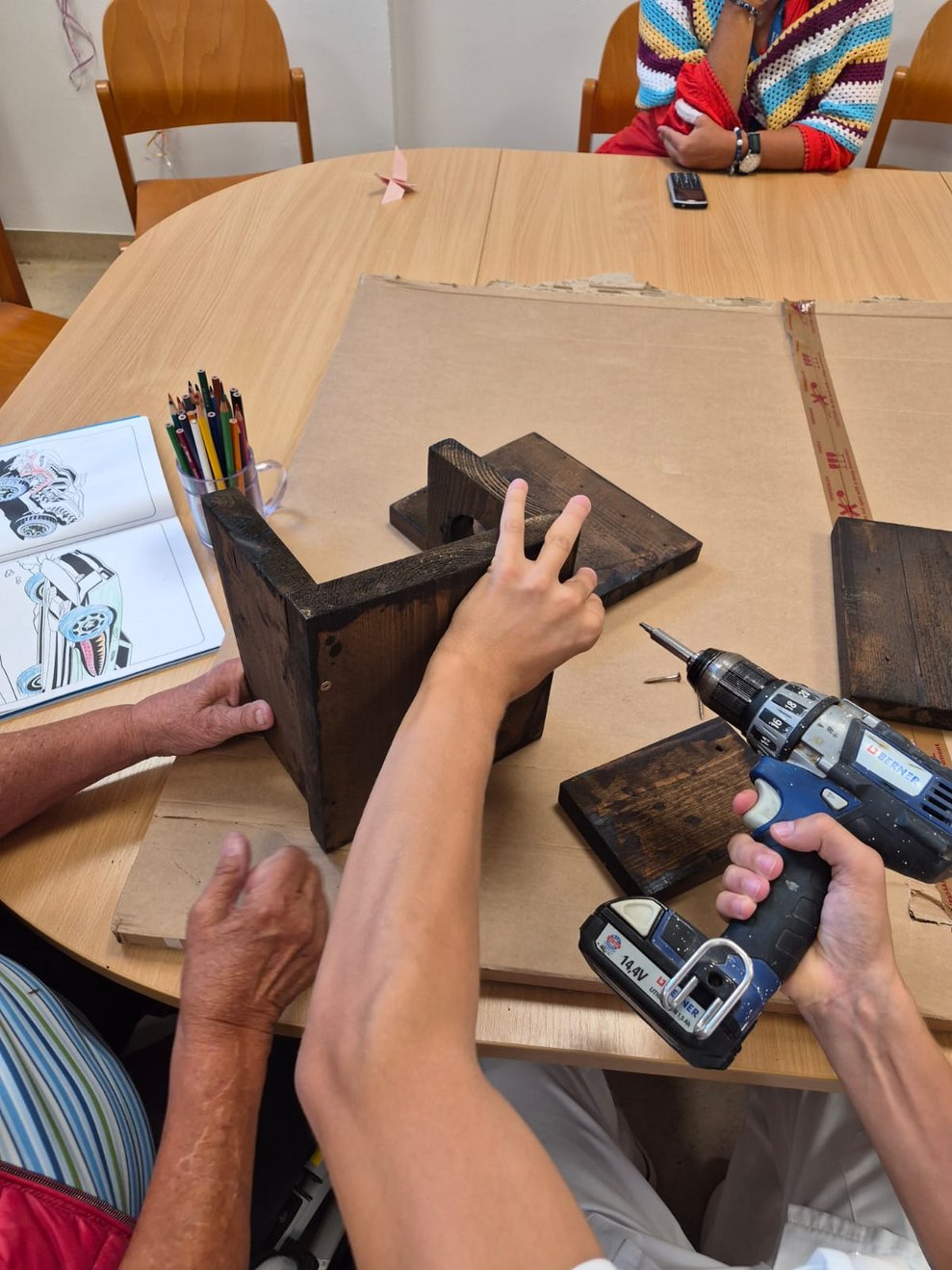 Hand hält Bohrmaschine und Holzbrett wird angebohrt.