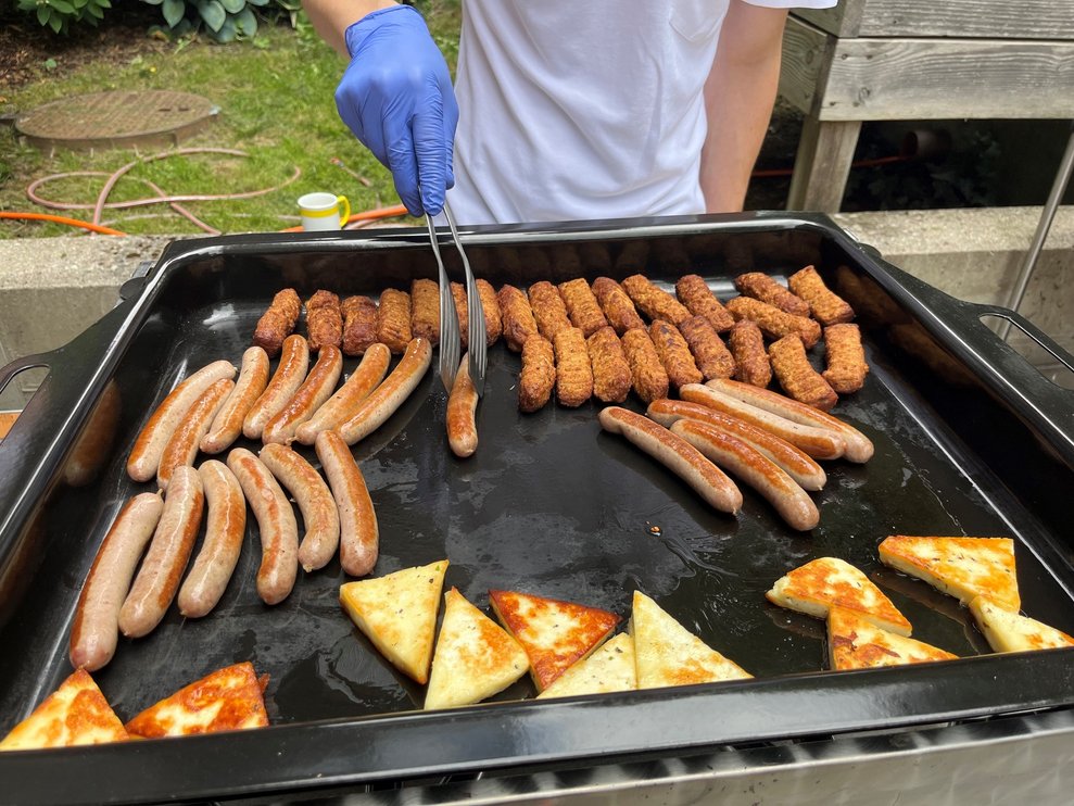Eine zweite Grillplatte, auf der gerade Würstchen, Cevapcici und Käse zubereitet wird.