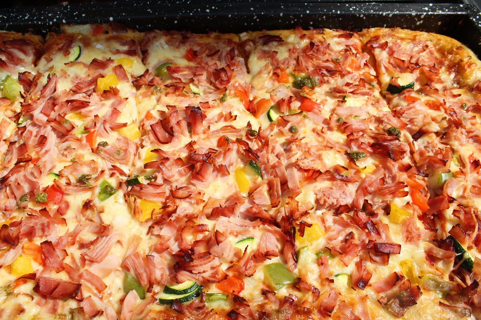 Nahaufnahme Pizza mit Schinkenstreifen und Gemüse.