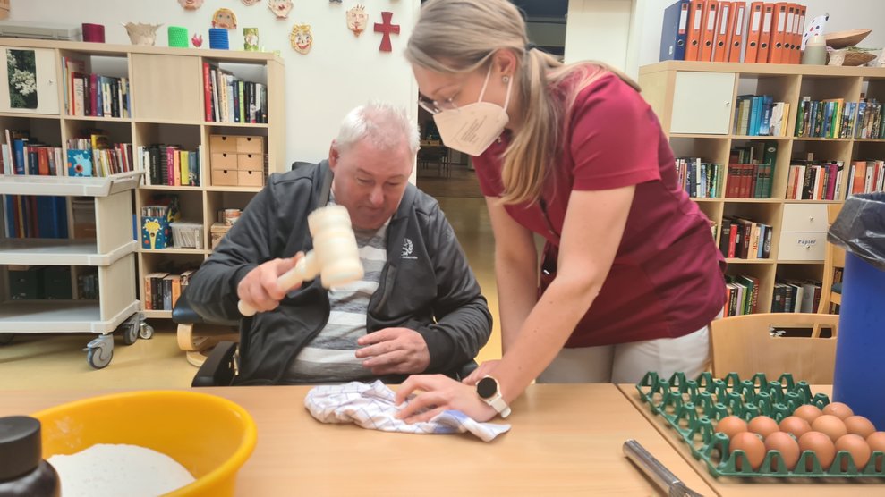 Herr V. zerteilt die Schokolade in kleinere Stücke und bekommt von Ergotherapeutin Kathy Unterstützung.
