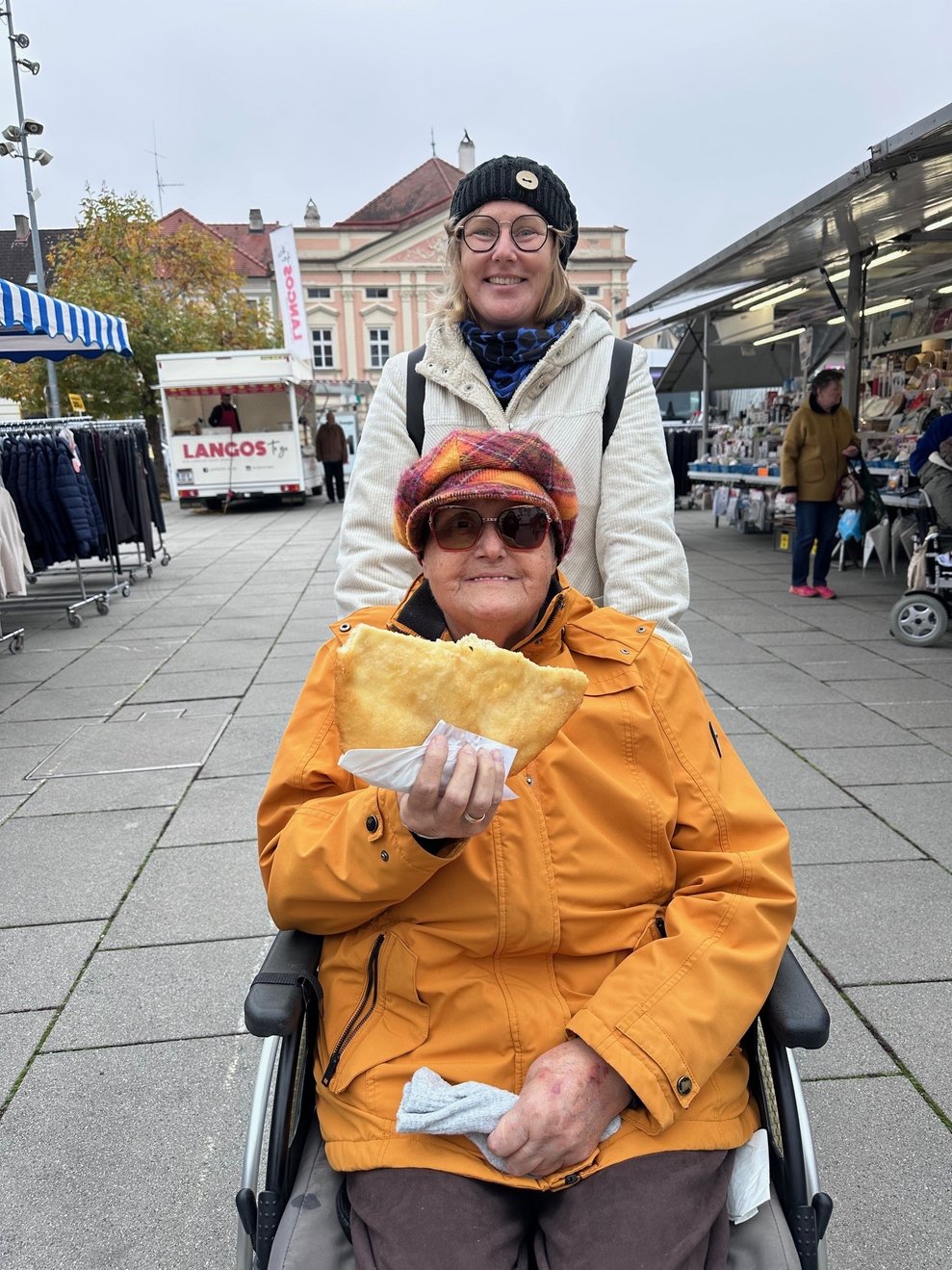 eine Dame im Rollstuhl mit einem Langos in der Hand