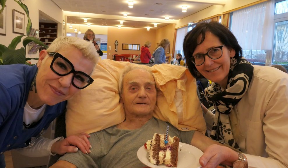 Zwei Damen gratulieren einem Herren zum Geburstag.