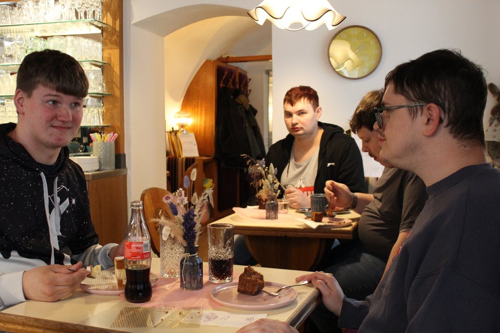 Mehrere Personen sitzen an zwei Tischen und essen Kuchen.