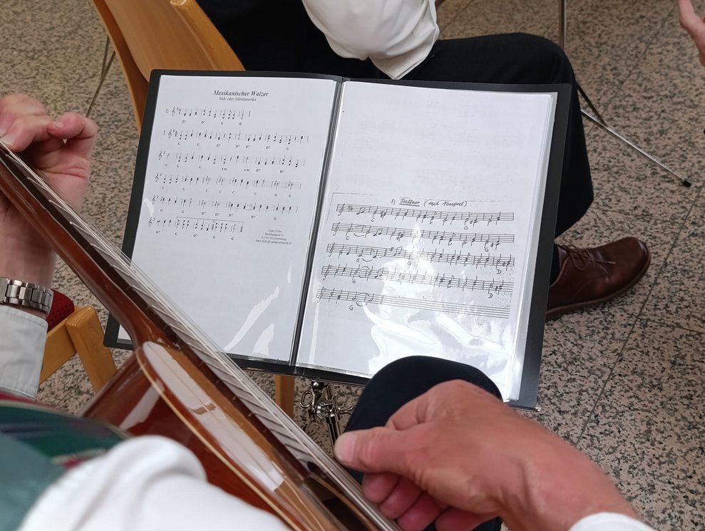 Hände spielen auf Gitarre. Notenheft auf Notenständer.