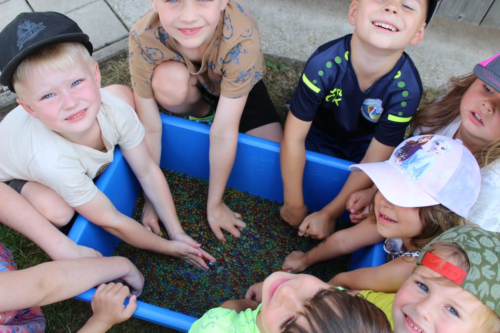 Kinder sitzen um ein kleines Waschbecken und spielen mit Aquaperlen.