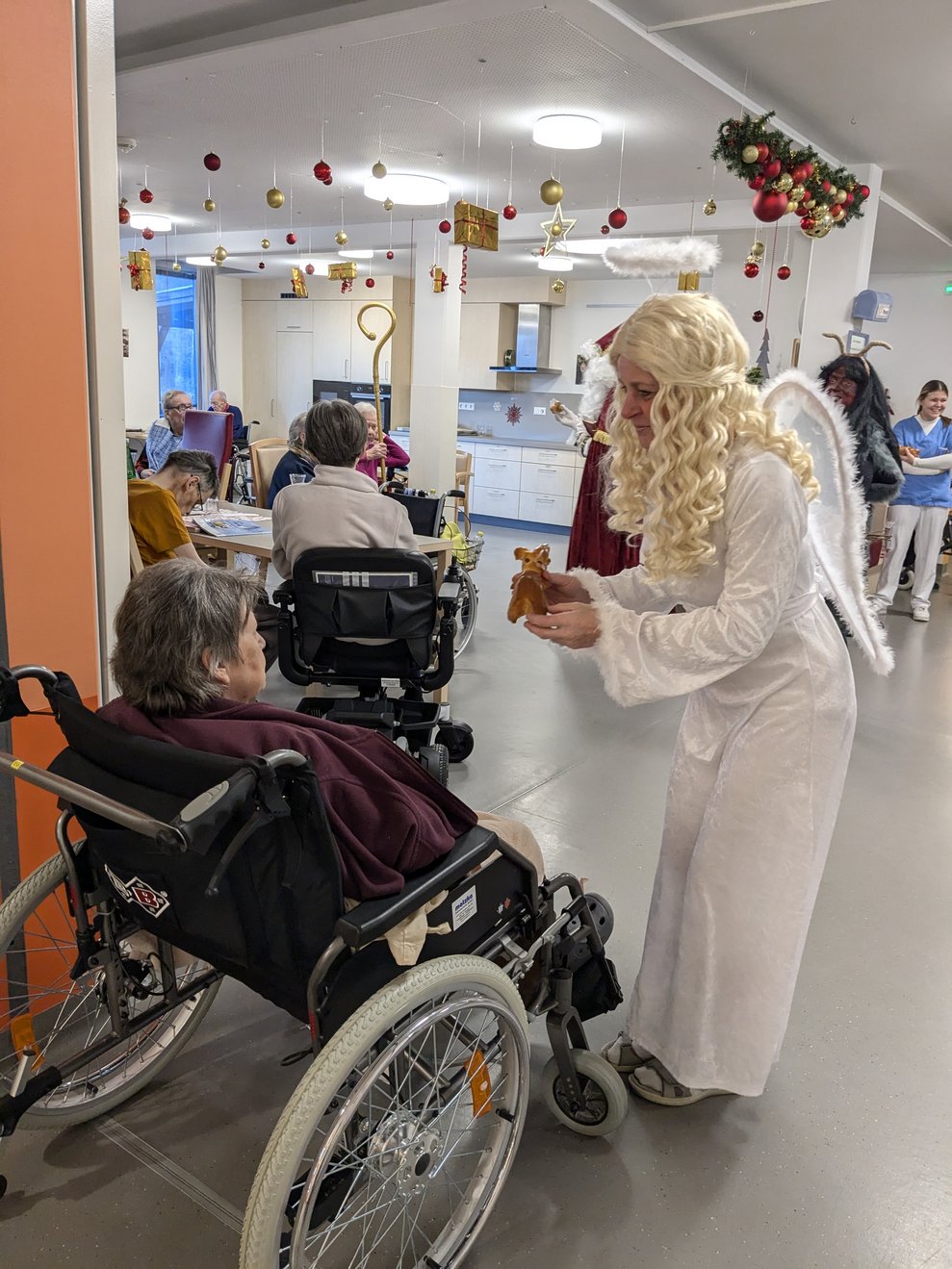 Das Christkind überreicht einer Dame einen Germteigkrampus.