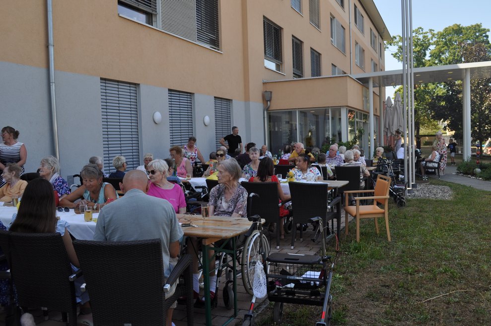 viele Menschen sitzen im Garten vor dem Pflegeheim beim italienischen Nachmittag