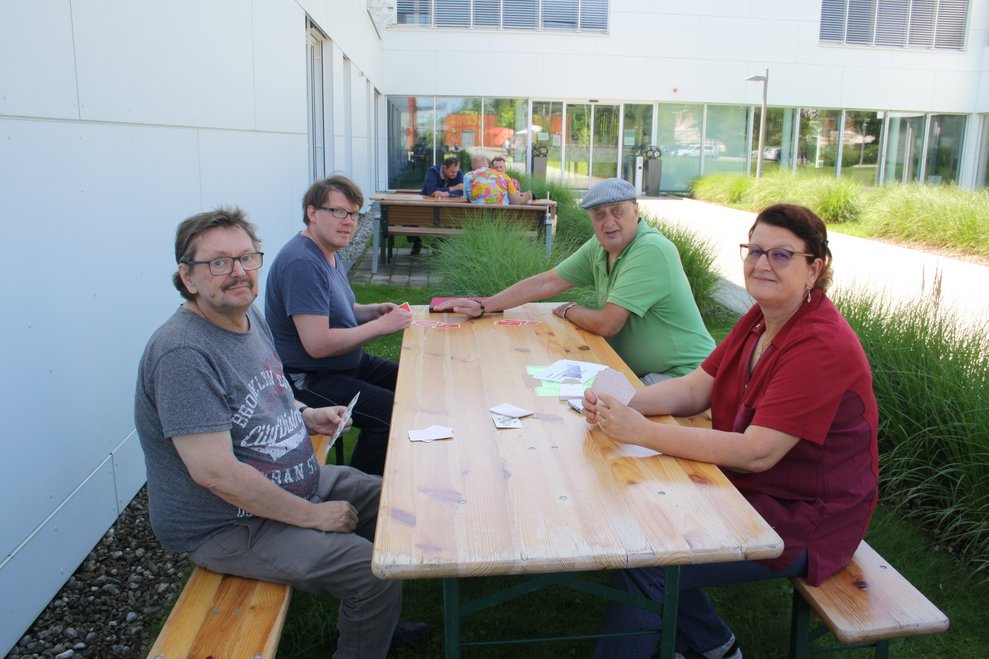 Personen sitzen bei einem Tisch und spielen Karten