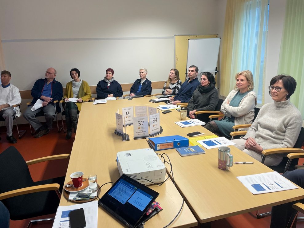Einige Personen sitzen um eine große Tischgruppe.