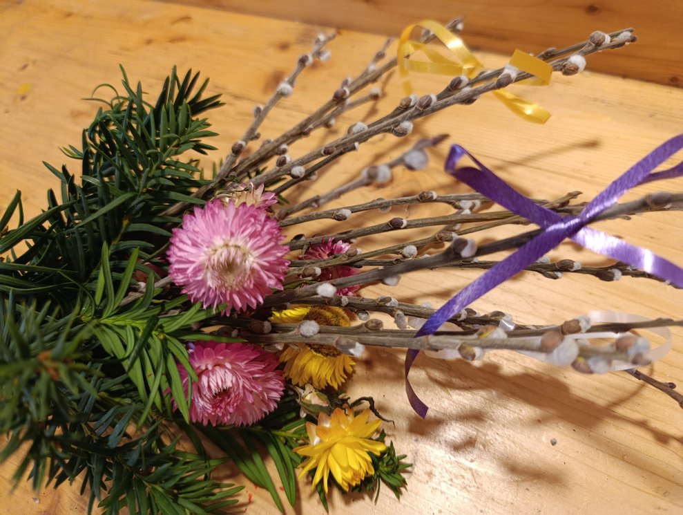 Gebundener Palmbuschen mit lila Schleife und Blumen.