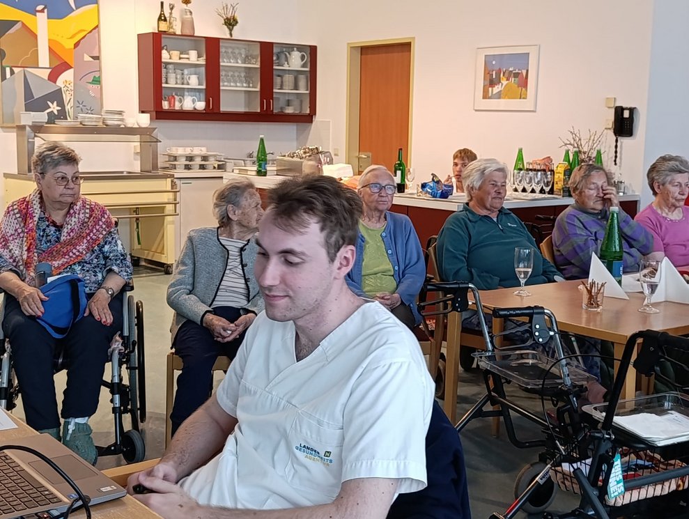 Viele BewohnerInnen bei der BewohnerInnenbesprechung. Mann sitzt beim Computer.