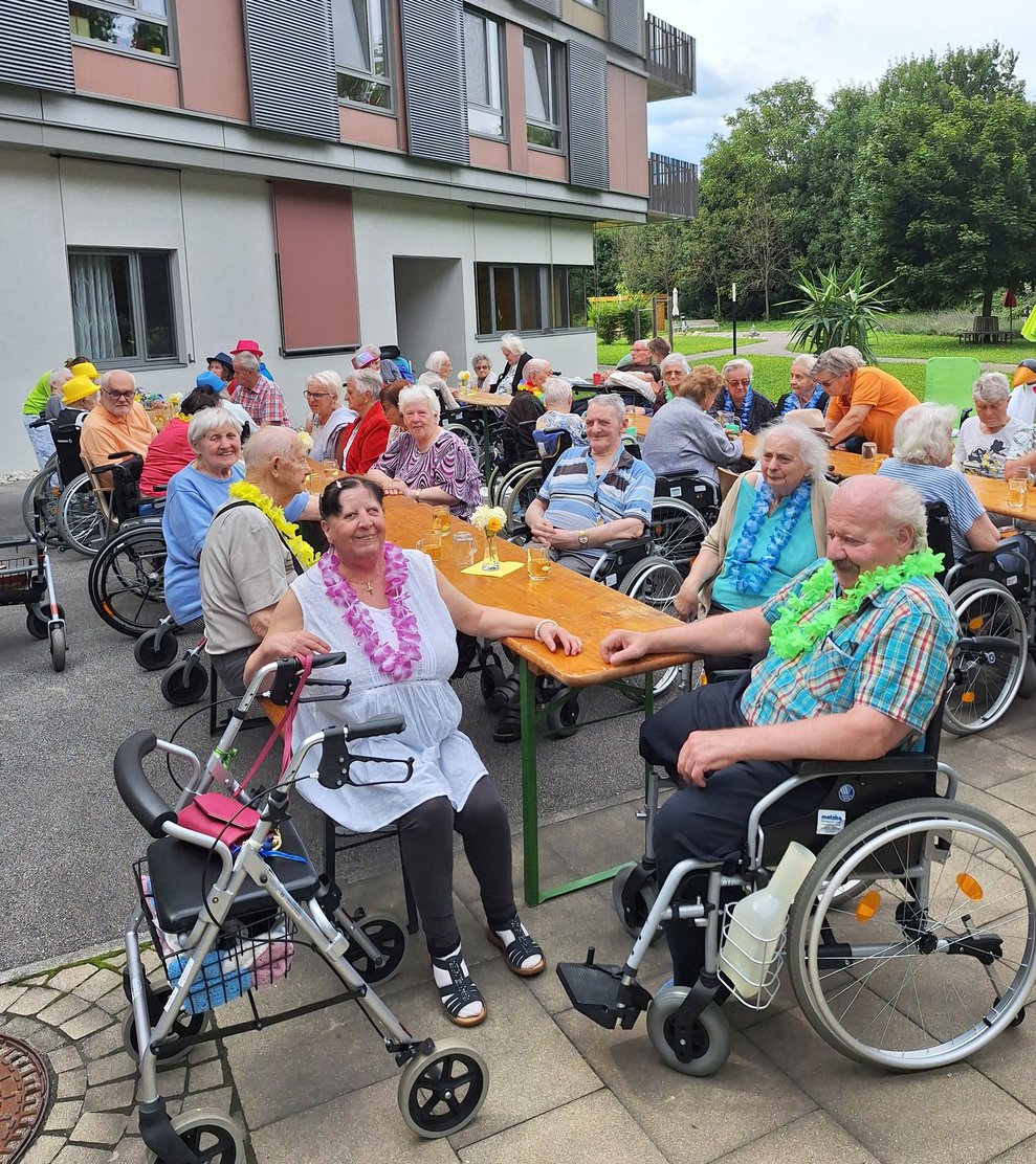 Zahlreiche BewohnerInnen, haupt- und ehrenamtliche MitarbeiterInnen sowie Angehörige, die zu Besuch da sind, haben sich auf den vorbereiteten Plätzen in unserem Garten eingefunden.