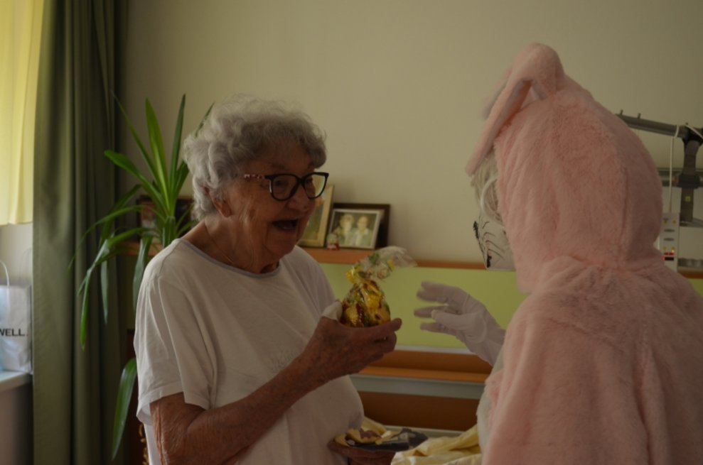 Eine Person, die als Osterhase verkleidet ist, gibt einer Bewohnerin Schokolade.