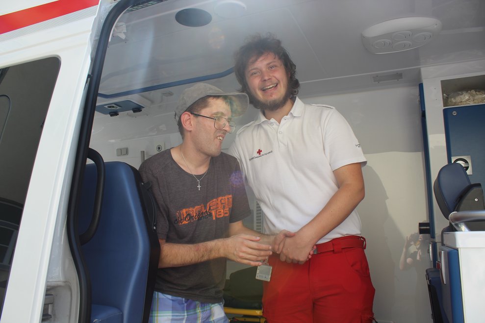 Ein Mitarbeiter des Roten Kreuz zeigt einer Person den Rettungskrankentransport.