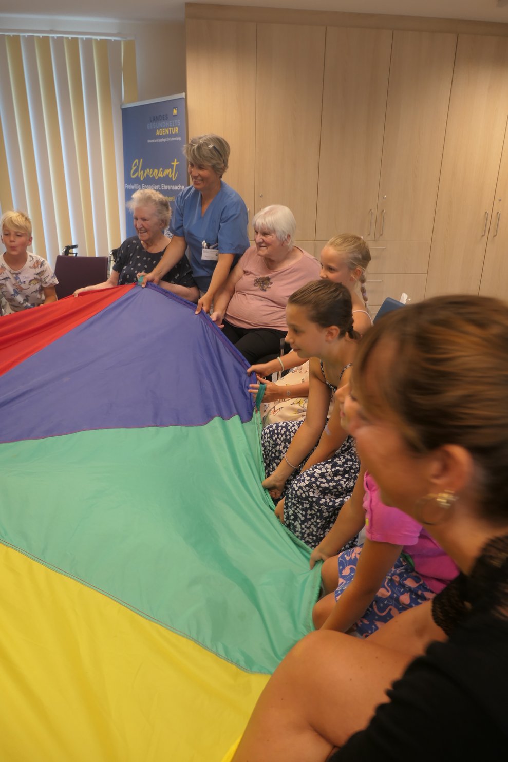 Die Kinder und SeniorInnen spielen mit dem Fallschirm und Luftballon.