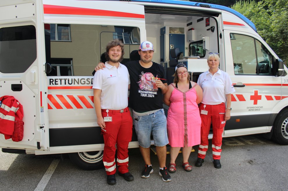 2 Mitarbeiter stehen mit zwei Personen vor dem Rettungskrankentransport.
