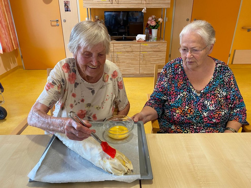 Zwei ältere Damen beim Bestreichen eines Apfelstrudels