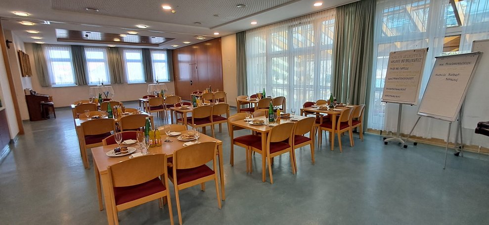 Festsaal mit gedeckte Tischt, Sesseln und zwei Tafeln mit Papier.