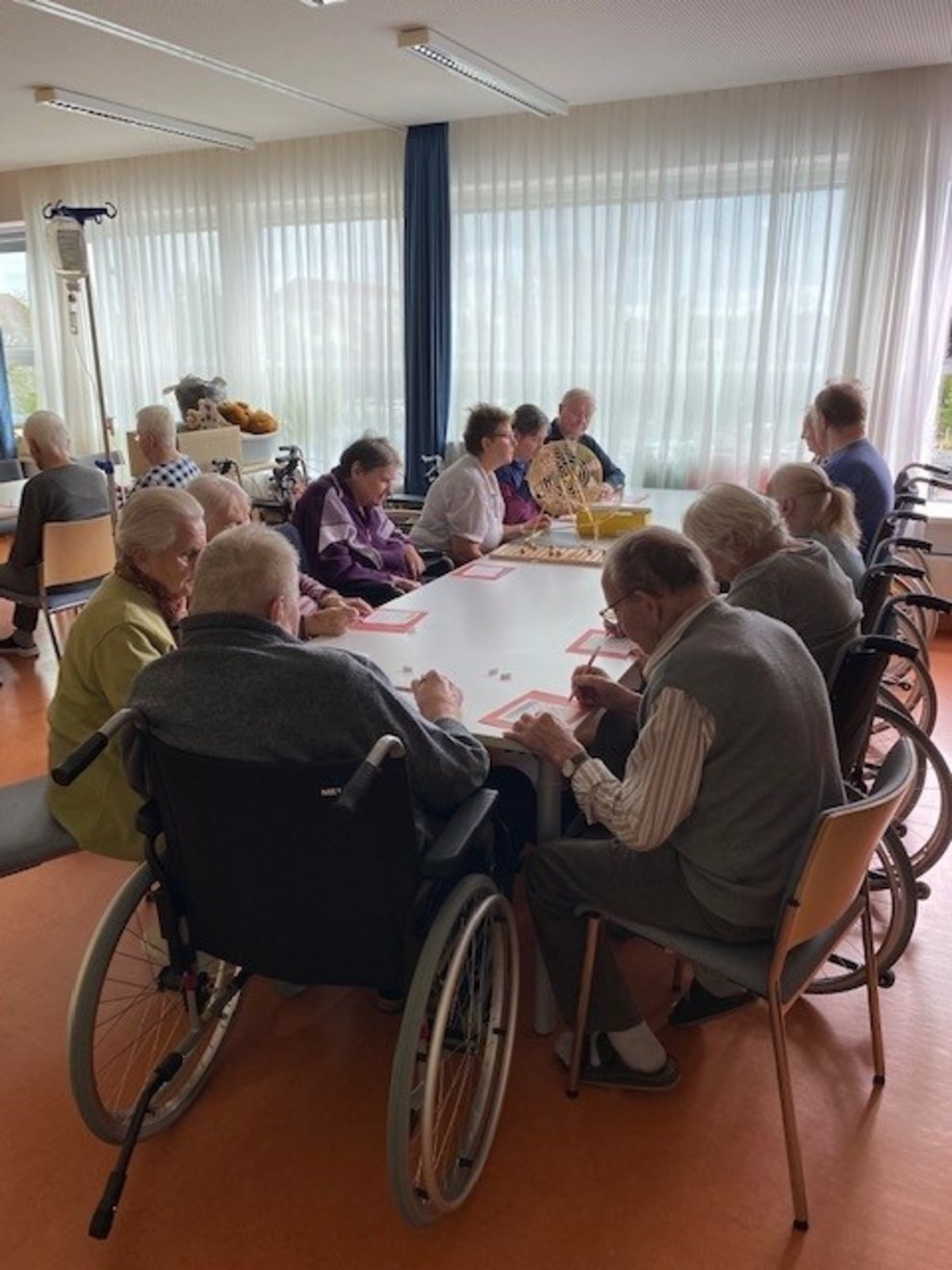 Bewohnerinnen und Bewohner sitzen beim Tisch und spielen Bingo
