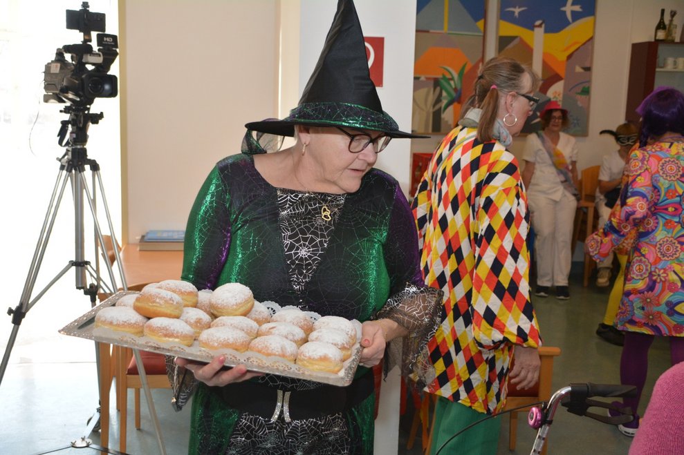 Frau mit Hexenhut hält Karton mit Krapfen.
