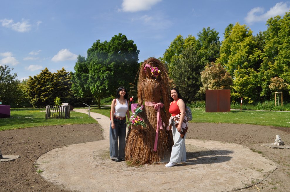 Zwei junge Damen bei einer großen Frauen Statue aus Ästen