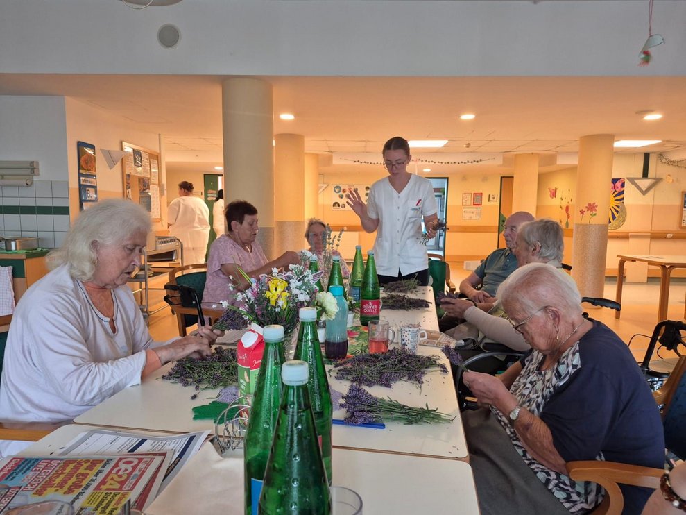 Praktikantin steht und hält Lavendel in der Hand. Bewohnerinnen beim Abrebeln vom Lavendel.