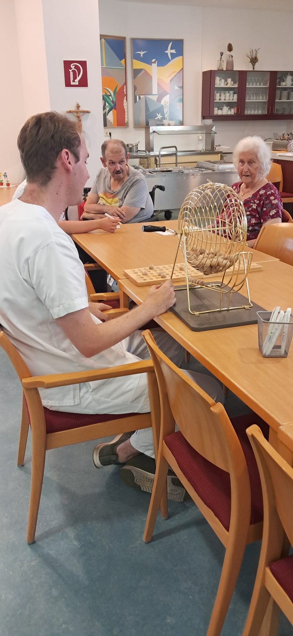 Mann (Aushilfskraft) und BewohnerIn beim Bingo spielen.