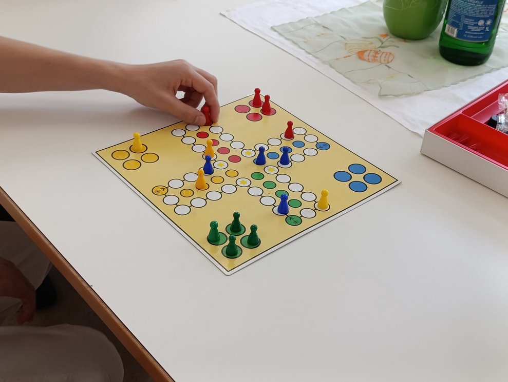 Hand hält Spielfigur beim Brettspiel "Mensch - ärgere - dich - nicht!". Spielfiguren auf Spielbrett.