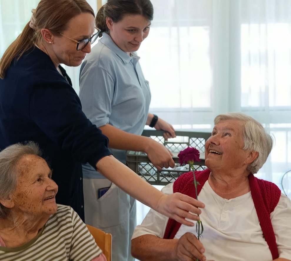 Pflege- Betreuungsmanagerin gibt Bewohnerin eine Nelke.