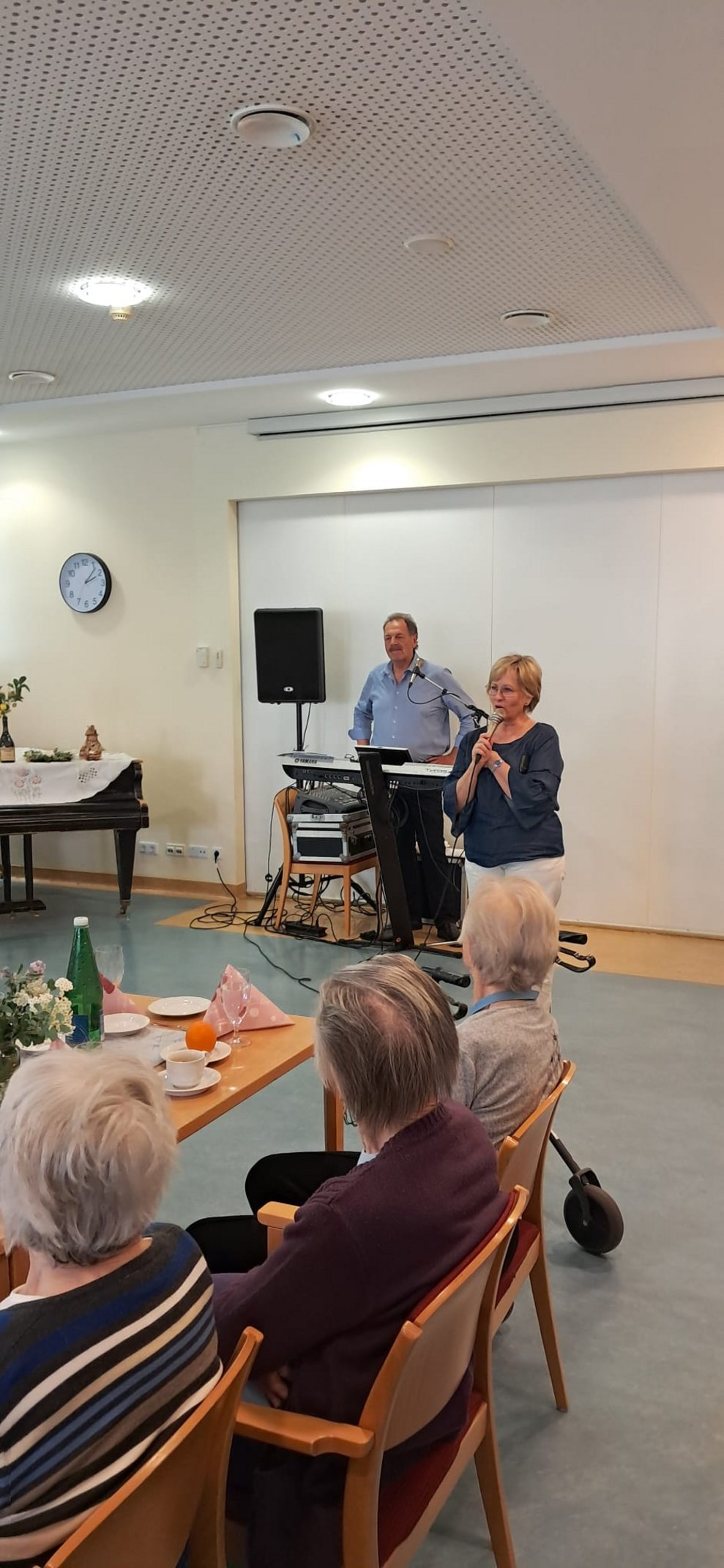 Pflegedirektorin redet ins Mikrofon. Im Hintergrund steht ein Mann mit Keyboard.