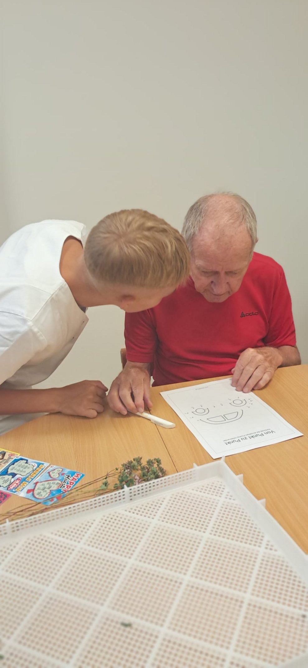 Bewohner beim Bild zeichnen und Mann (FSJ) schaut Bewohner an.