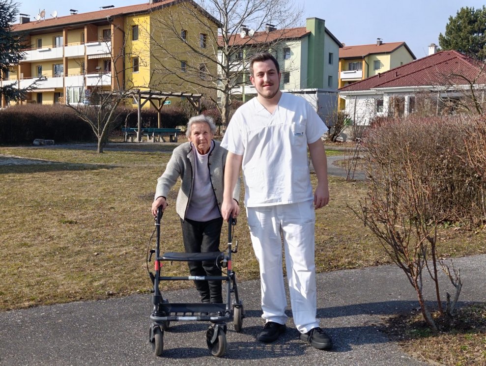 Bewohnerin mit Rollator und Mann beim Spaziergang.