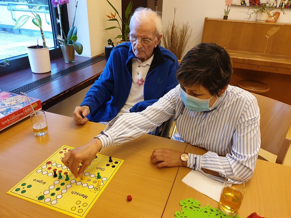 Bewohner und eine Betreuerin spielen "Mensch ärger dich nicht".