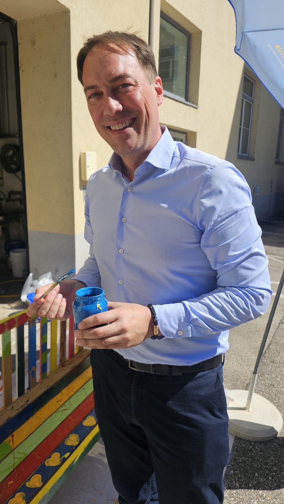 Ein Mann hat einen Pinsel in der Hand um eine Bank zu bemalen