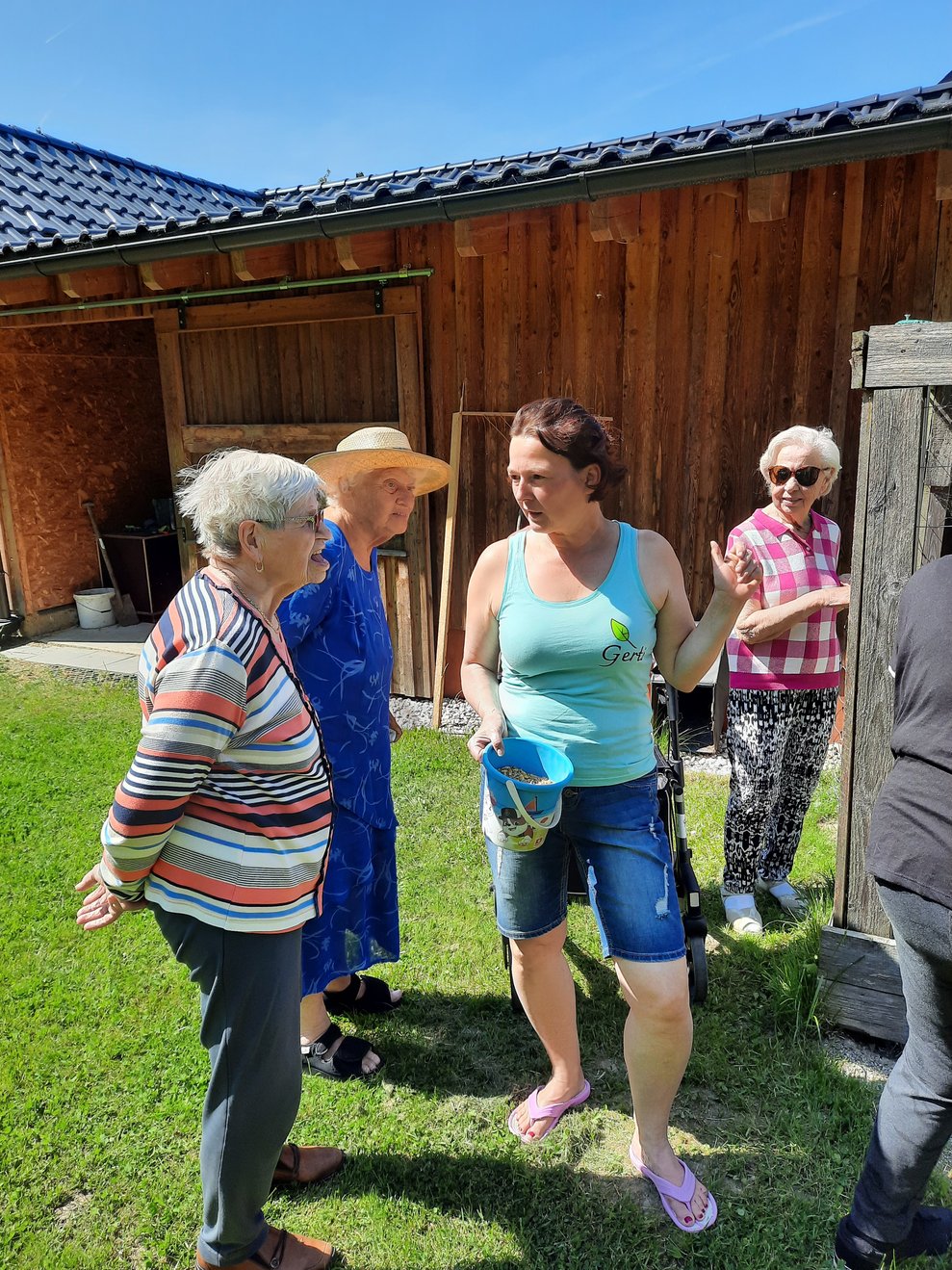 Einige Personen stehen vor einem Holzschuppen in der Wiese.