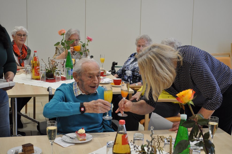 ein älterer Herr und eine Frau stoßen mit Sekt Orange an