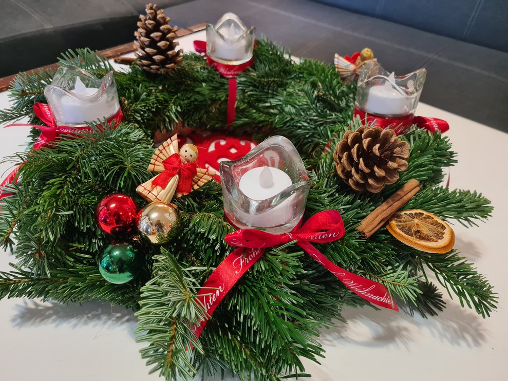 Adventkranz mit roten, goldenen und grünen Kugeln.