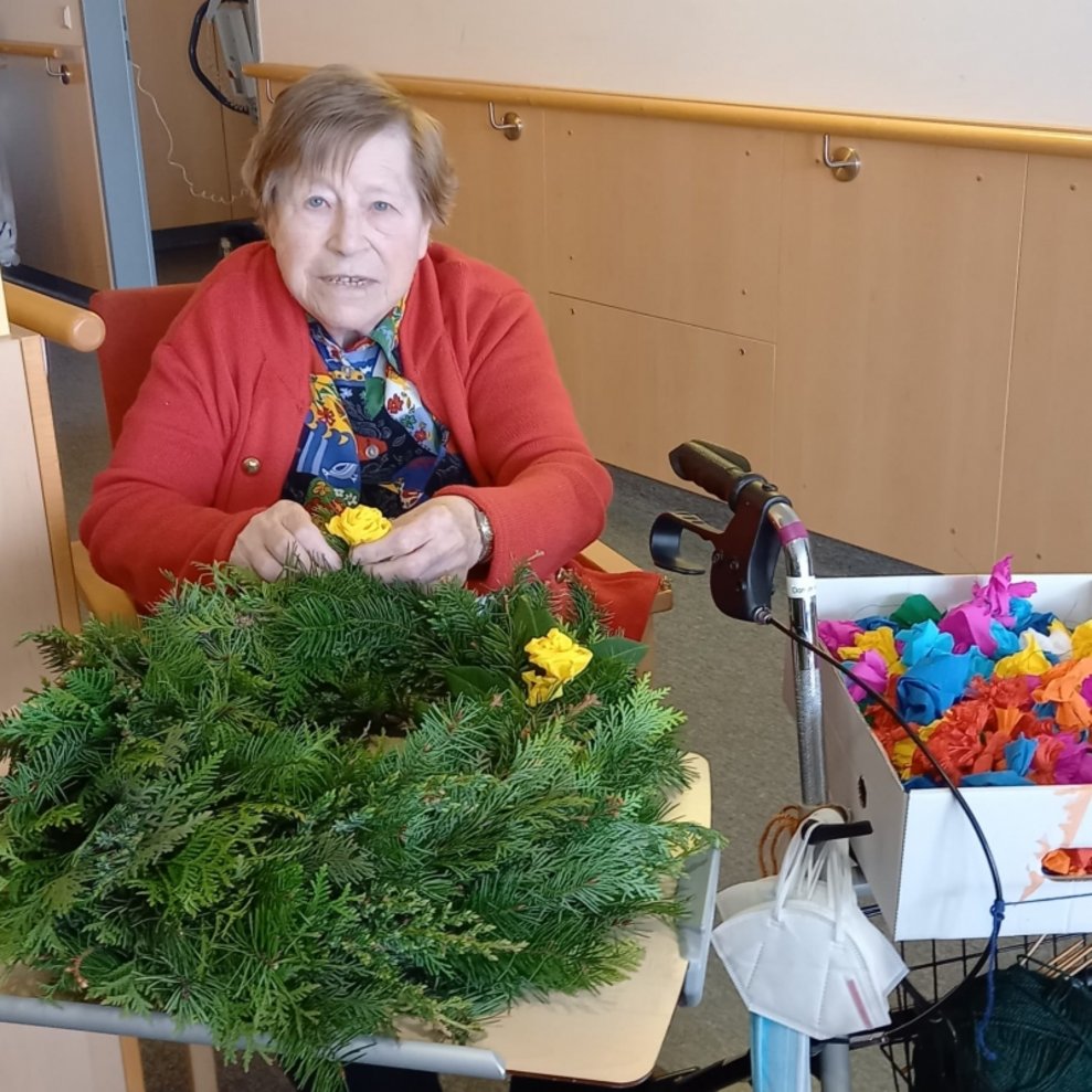 Eine Bewohnerin dekoriert einen Kranz mit Rosen.