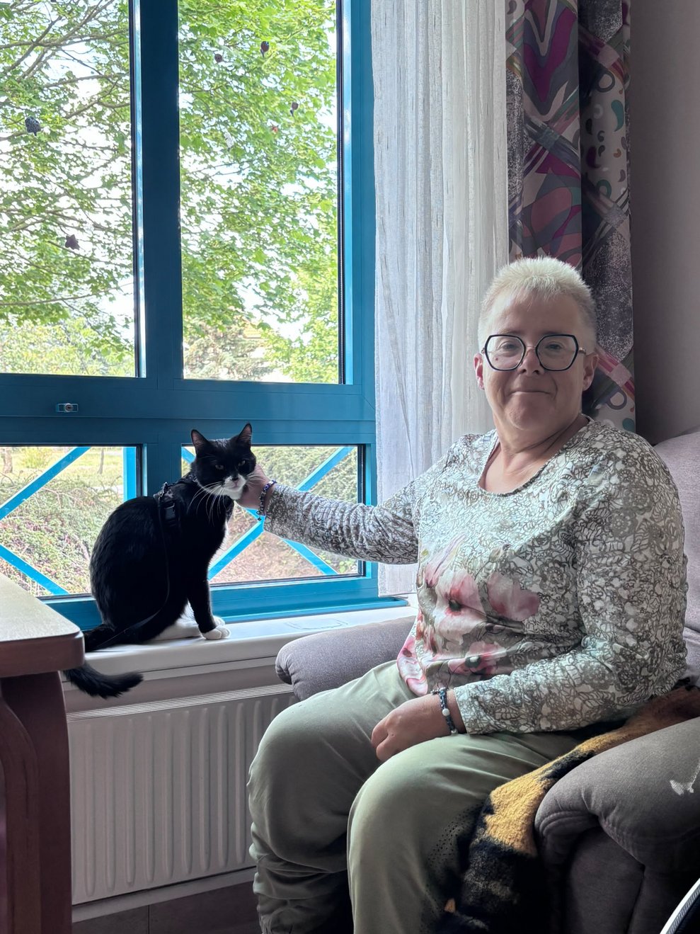 Bewohnerin streichelt Kater der auf Fensterbrett sitzt.