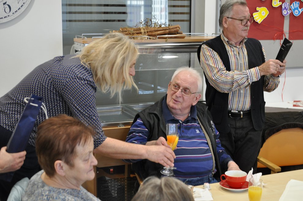 ein älterer Herr und eine Frau stoßen mit Sekt Orange an