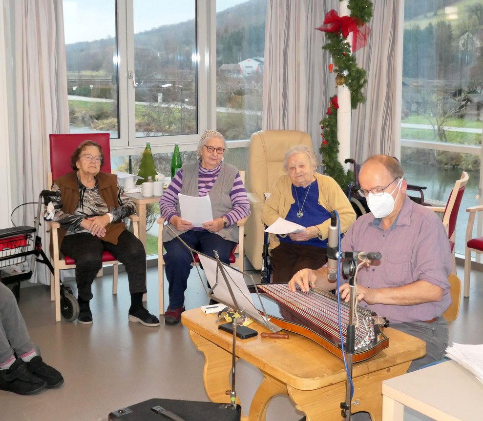 Ein Mann spielt Zither, im Hintergrund sitzen drei Damen.