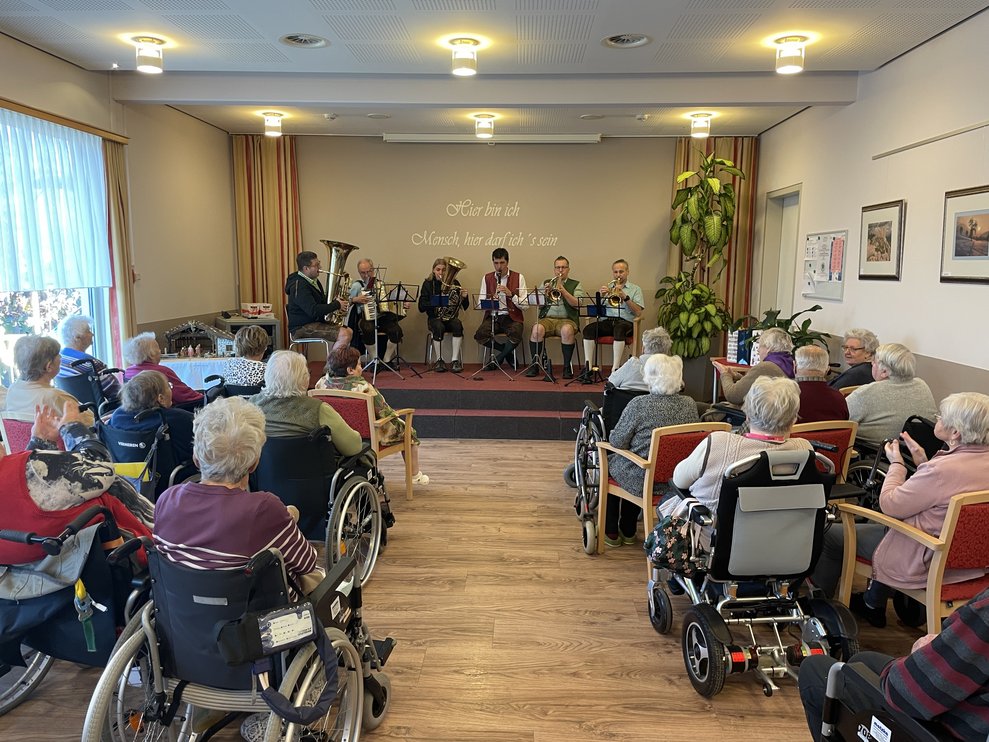 BewohnerInnen sitzen im Festsaal, auf der Bühne spielen die Musikanten