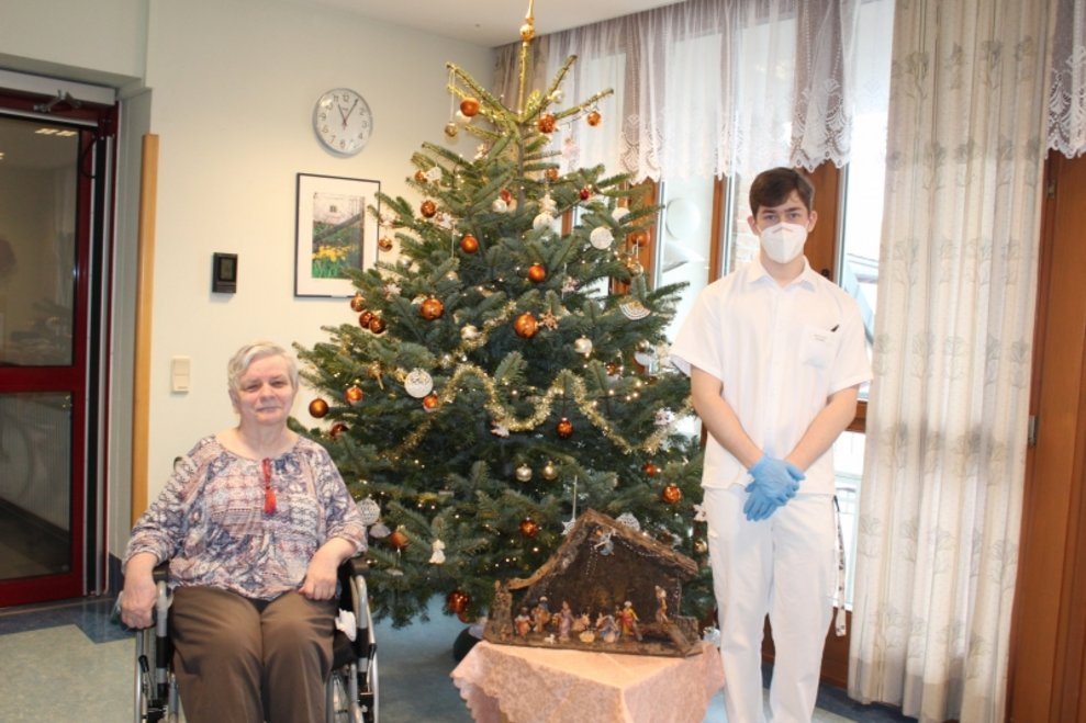 Ein Zivildiener und eine Bewohnerin stehen beim Christbaum.