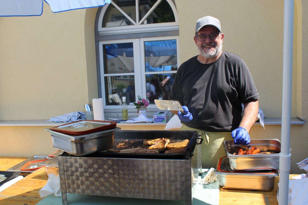 Eine Person steht vor einem Grill und grillt Würstel