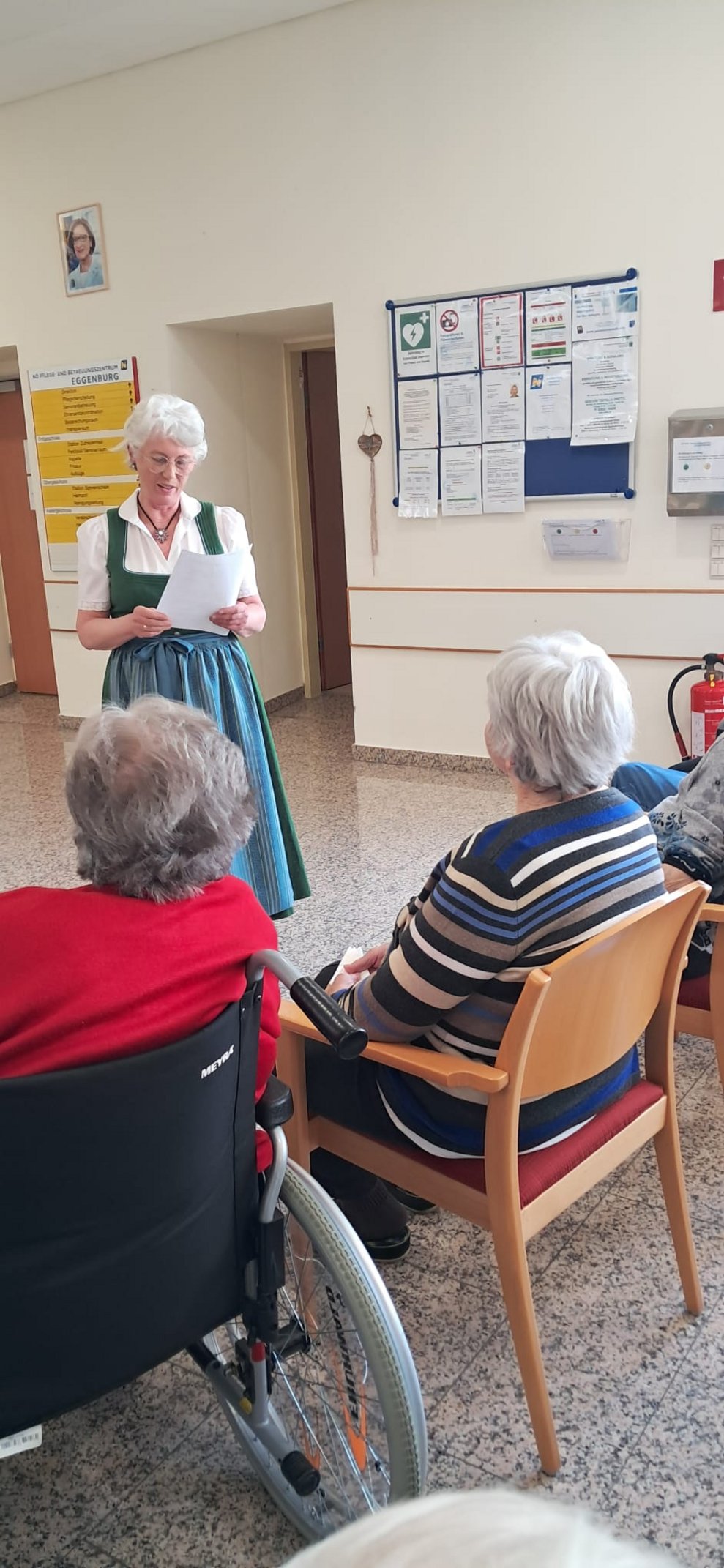 Frau steht. Sitzende Bewohnerinnen.