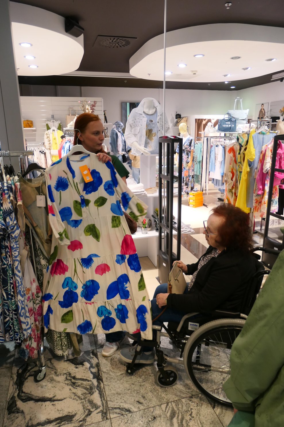Frau zeigt Bewohnerin buntes Kleid.