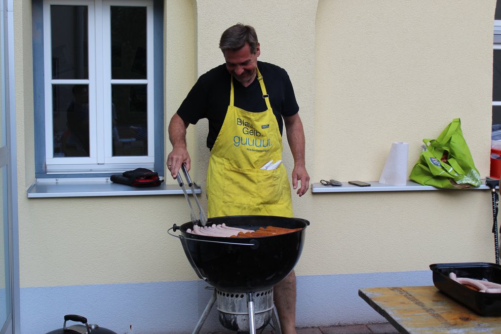 Eine Person steht am Grill und grillt Würstchen.