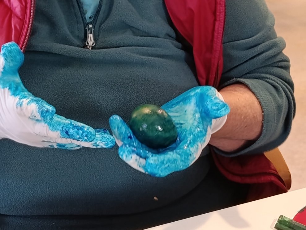 Hände mit Plastikhandschuhen halten gefärbtes Ei.