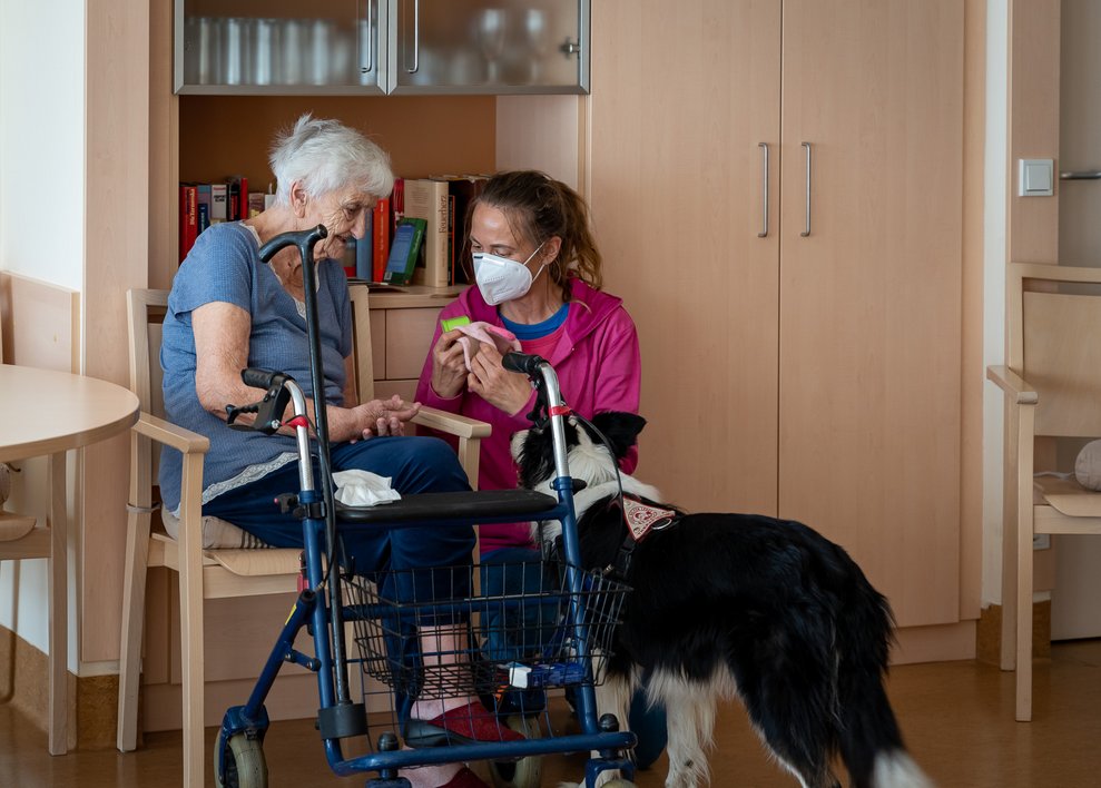 Eine Bewohnerin und eine Betreuerin sitzen bei einem Hund.
